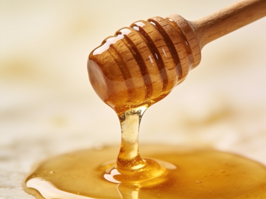 Golden honey dripping from a wooden dipper